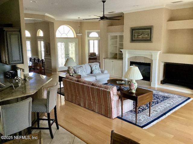 living room with built in features, a glass covered fireplace, french doors, and light wood-style flooring