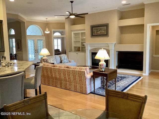 living room featuring built in shelves, french doors, a fireplace, light wood-style flooring, and ornamental molding