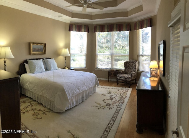 bedroom with a tray ceiling, crown molding, and light wood-style flooring