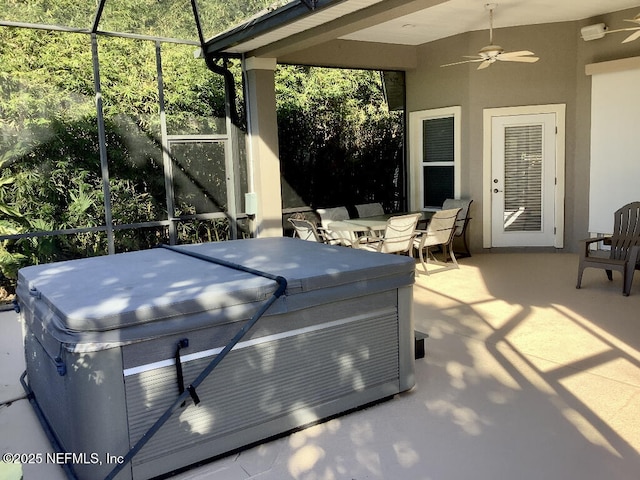 view of patio featuring glass enclosure, outdoor dining area, a ceiling fan, and a hot tub