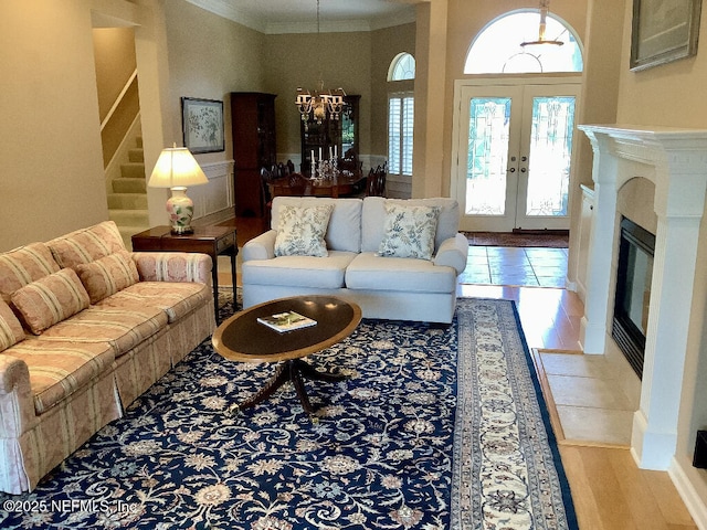 living room with light wood finished floors, a fireplace with flush hearth, ornamental molding, stairs, and french doors