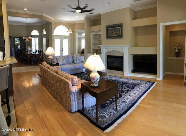 living room with a tiled fireplace, light wood-style flooring, crown molding, french doors, and built in shelves