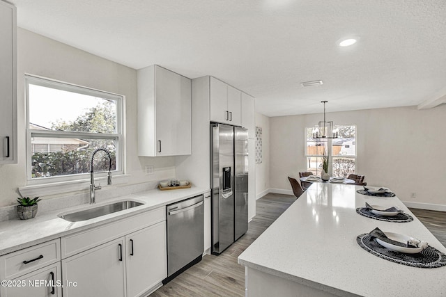 kitchen featuring appliances with stainless steel finishes, pendant lighting, white cabinetry, sink, and light wood-type flooring