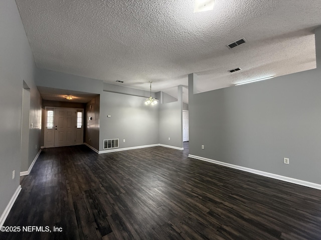 empty room with dark wood-type flooring, a chandelier, and a textured ceiling