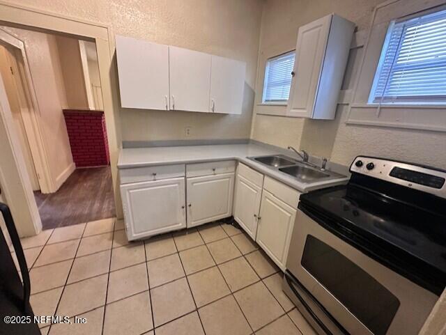 kitchen with electric stove, white cabinetry, sink, and light tile patterned floors