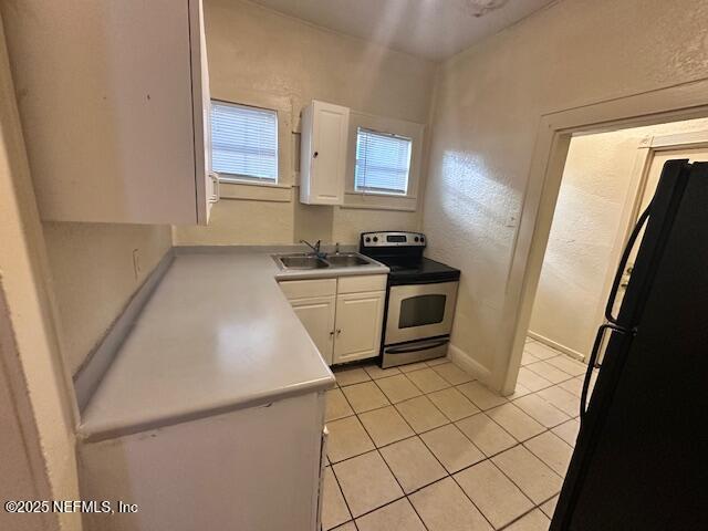 kitchen featuring sink, light tile patterned floors, black refrigerator, white cabinets, and stainless steel electric range oven