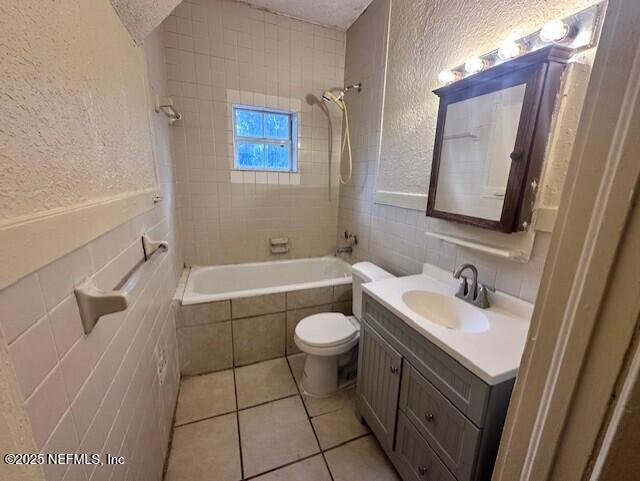 full bathroom with tiled shower / bath, tile walls, tile patterned flooring, vanity, and toilet