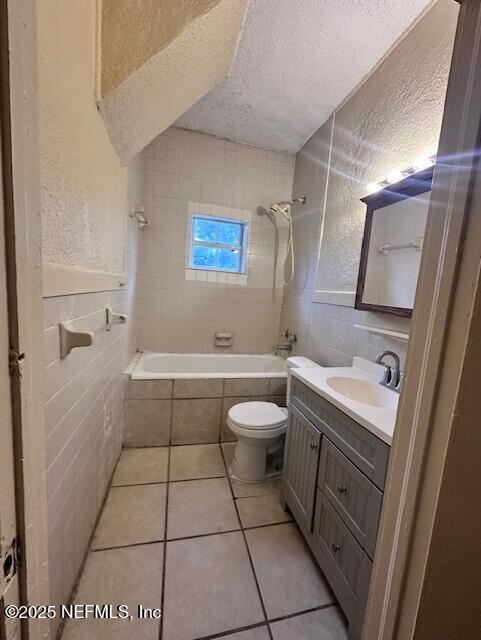 full bathroom featuring tile walls, tile patterned flooring, vanity, toilet, and a textured ceiling