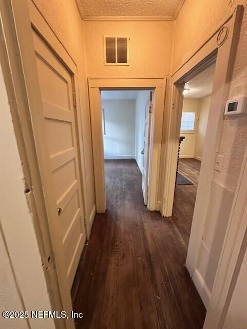 corridor with dark wood-type flooring, crown molding, and a textured ceiling