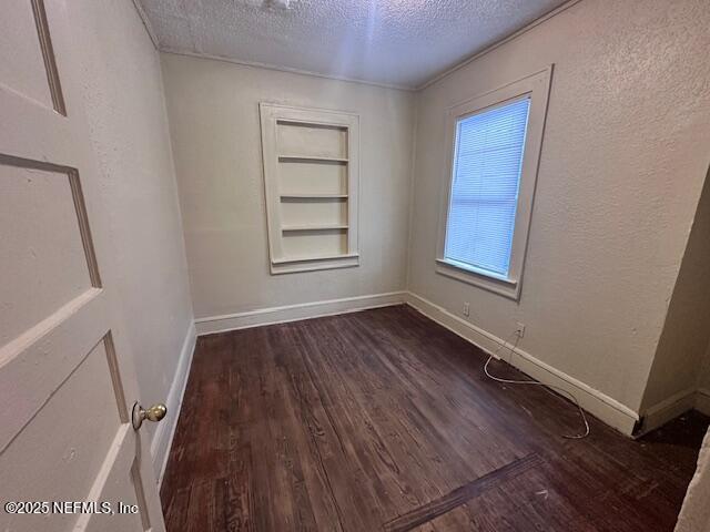 spare room with built in features, dark hardwood / wood-style flooring, and a textured ceiling