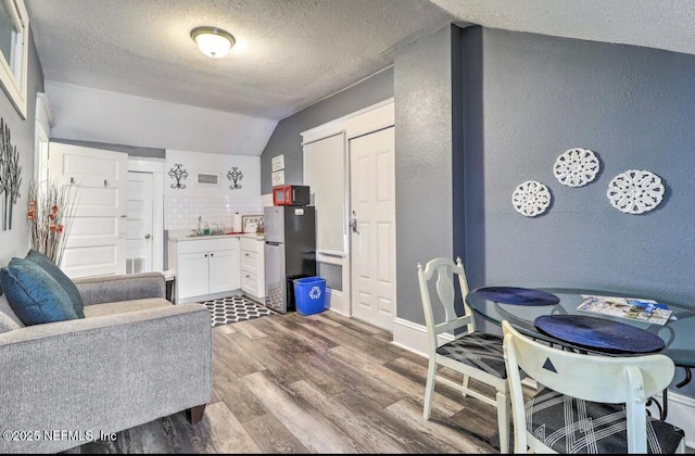 dining area with sink, light hardwood / wood-style floors, vaulted ceiling, and a textured ceiling