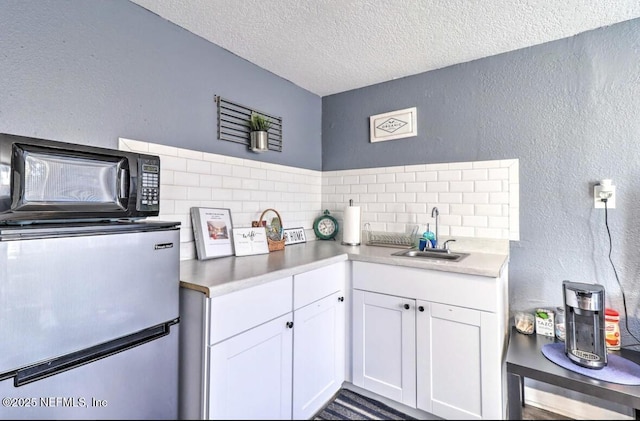 kitchen featuring white cabinets, sink, a textured ceiling, and stainless steel fridge