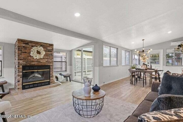 living room featuring a brick fireplace, a notable chandelier, vaulted ceiling, and light hardwood / wood-style floors