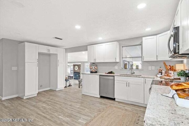 kitchen featuring appliances with stainless steel finishes, white cabinetry, sink, light hardwood / wood-style floors, and light stone countertops