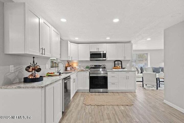 kitchen with appliances with stainless steel finishes, white cabinetry, sink, light hardwood / wood-style floors, and a textured ceiling