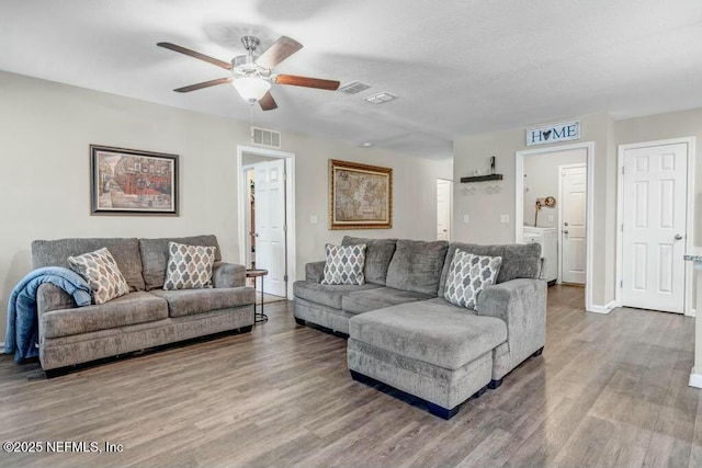 living room featuring washer / clothes dryer, visible vents, ceiling fan, wood finished floors, and baseboards