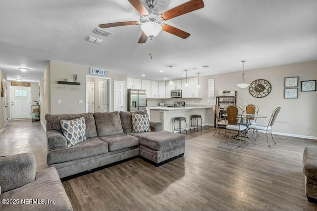 living area featuring ceiling fan, dark wood finished floors, visible vents, and baseboards