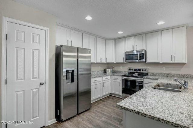 kitchen with light stone counters, a sink, white cabinets, appliances with stainless steel finishes, and light wood finished floors