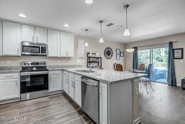 kitchen with visible vents, white cabinets, decorative light fixtures, a peninsula, and stainless steel appliances