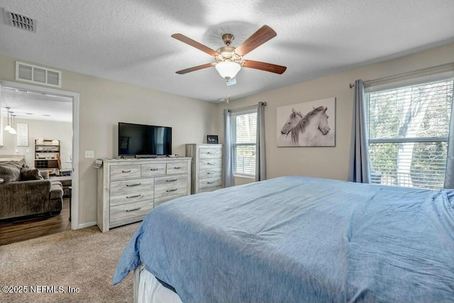 bedroom featuring light carpet, a ceiling fan, visible vents, and a textured ceiling