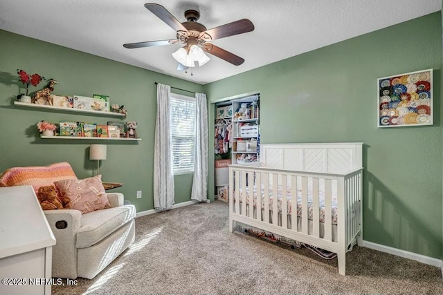 carpeted bedroom with a nursery area, baseboards, and a ceiling fan