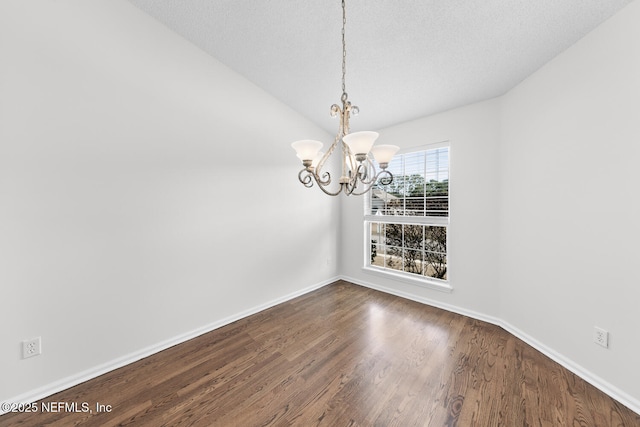 unfurnished dining area with an inviting chandelier, lofted ceiling, hardwood / wood-style floors, and a textured ceiling