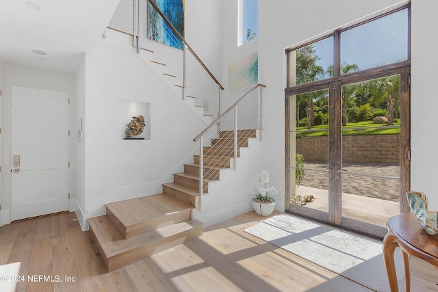 foyer entrance featuring a towering ceiling, light hardwood / wood-style floors, and french doors