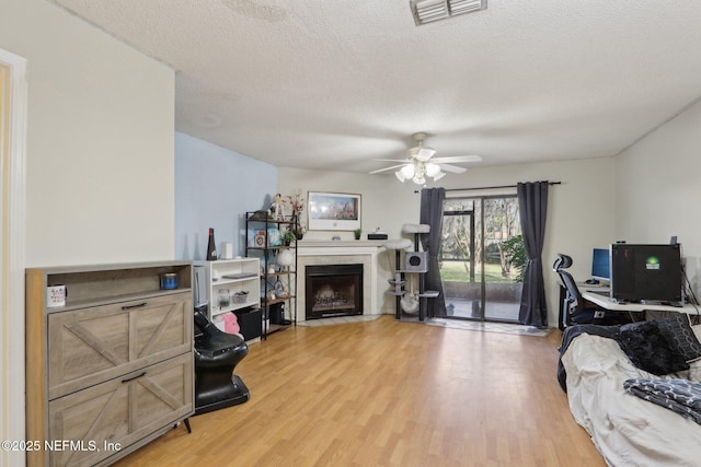 living room featuring a tile fireplace, a textured ceiling, ceiling fan, and light hardwood / wood-style floors