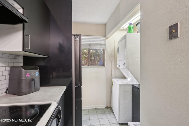 laundry area featuring stacked washing maching and dryer, a textured ceiling, and light tile patterned floors