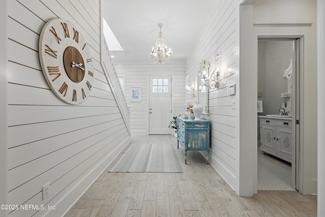 hall with a chandelier, a sink, light wood-style flooring, and wooden walls