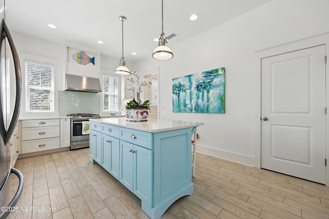 kitchen with appliances with stainless steel finishes, blue cabinets, ventilation hood, light countertops, and light wood-style floors