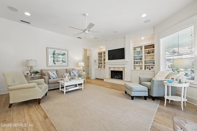 living area with a fireplace with raised hearth, recessed lighting, a ceiling fan, visible vents, and light wood-style floors