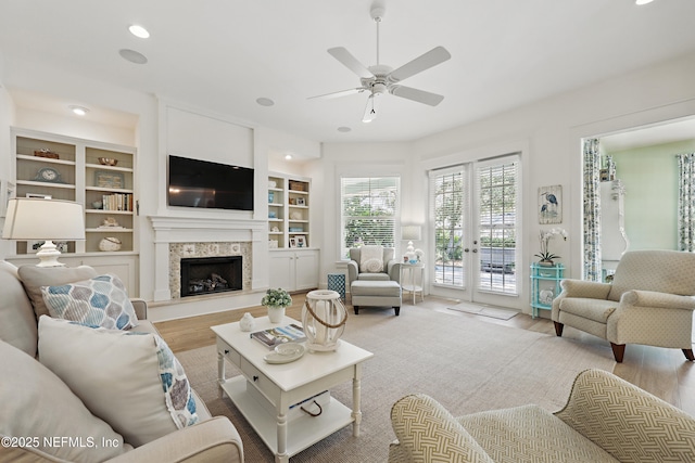 living room featuring a fireplace with raised hearth, ceiling fan, wood finished floors, built in shelves, and recessed lighting