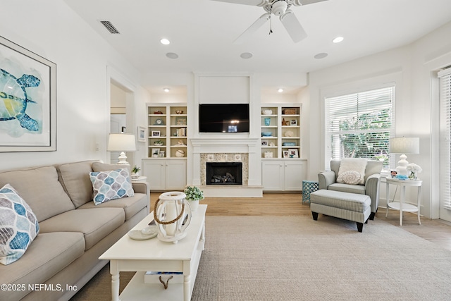 living room featuring visible vents, a fireplace with raised hearth, a ceiling fan, and recessed lighting