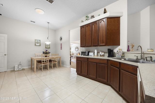 kitchen featuring sink, light tile patterned floors, hanging light fixtures, dark brown cabinets, and a textured ceiling