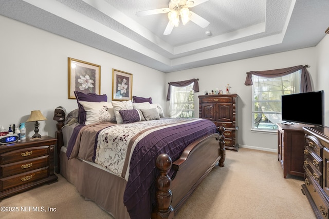 bedroom with light colored carpet, a tray ceiling, multiple windows, and a textured ceiling