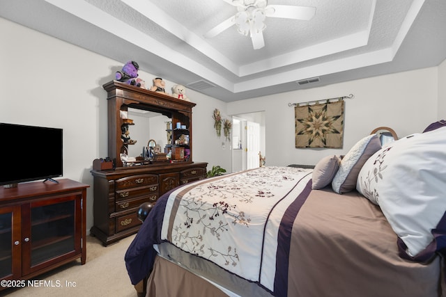 bedroom with ceiling fan, light carpet, a textured ceiling, and a tray ceiling