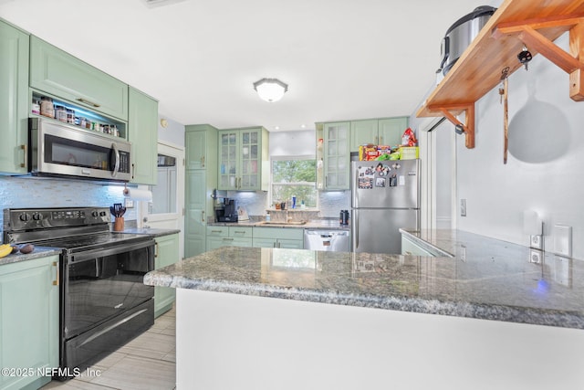 kitchen with appliances with stainless steel finishes, green cabinetry, sink, kitchen peninsula, and light stone countertops