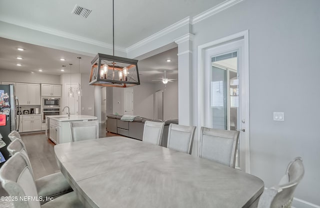 dining space with dark wood-type flooring, sink, ornamental molding, ceiling fan, and decorative columns