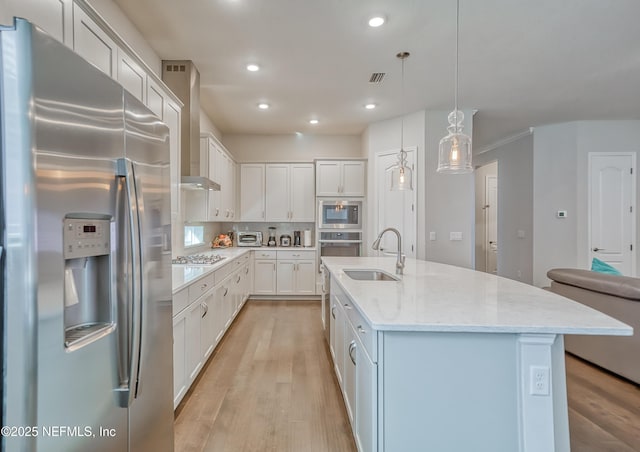 kitchen featuring pendant lighting, white cabinetry, sink, stainless steel appliances, and a center island with sink