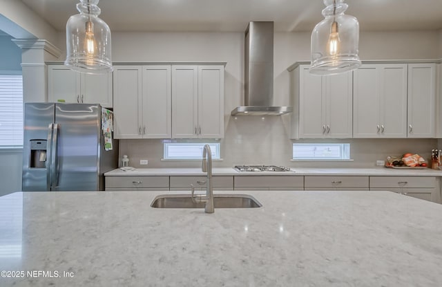 kitchen featuring sink, light stone counters, white cabinetry, stainless steel appliances, and wall chimney range hood