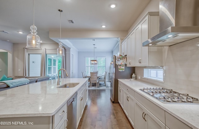 kitchen with sink, a center island with sink, pendant lighting, stainless steel appliances, and wall chimney range hood