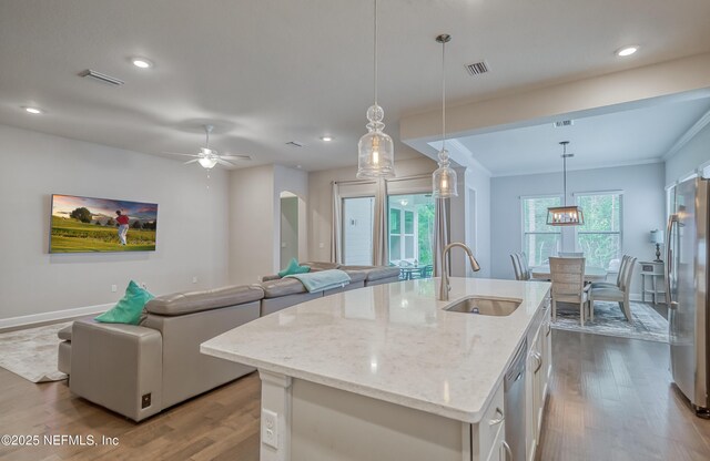 kitchen with sink, pendant lighting, stainless steel appliances, light stone countertops, and a kitchen island with sink