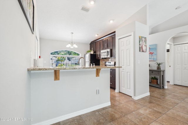 kitchen featuring appliances with stainless steel finishes, pendant lighting, a breakfast bar area, decorative backsplash, and dark brown cabinets