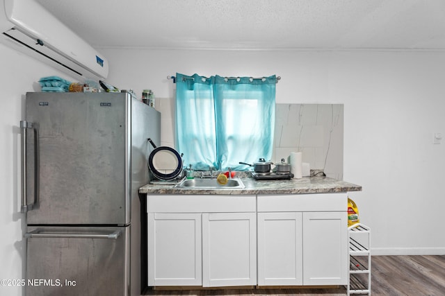 kitchen with sink, stainless steel fridge, a wall mounted AC, and white cabinets