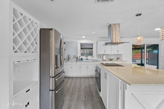 kitchen with stainless steel appliances, a center island, island range hood, white cabinets, and decorative light fixtures