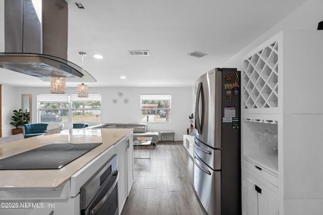 kitchen with pendant lighting, hardwood / wood-style flooring, appliances with stainless steel finishes, island range hood, and white cabinets