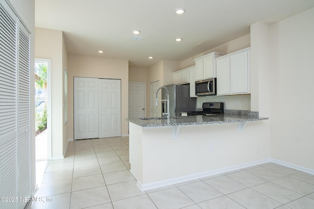 kitchen with light tile patterned floors, white cabinetry, stainless steel appliances, stone countertops, and kitchen peninsula