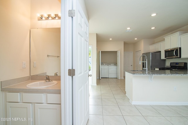 kitchen featuring sink, dark stone countertops, appliances with stainless steel finishes, washing machine and dryer, and white cabinets