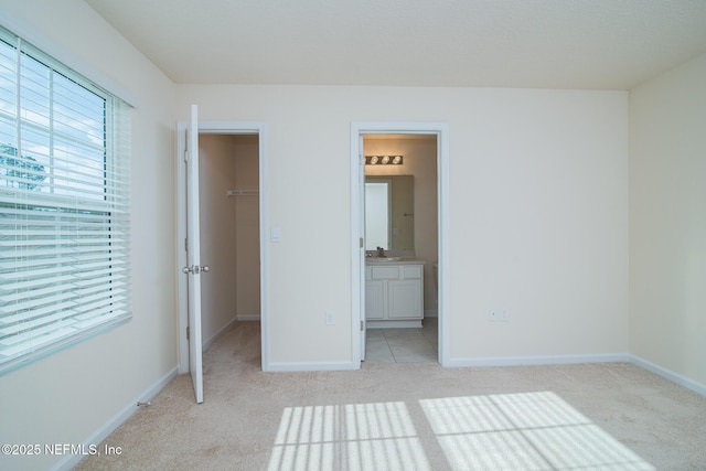 unfurnished bedroom featuring multiple windows, sink, a spacious closet, and light colored carpet